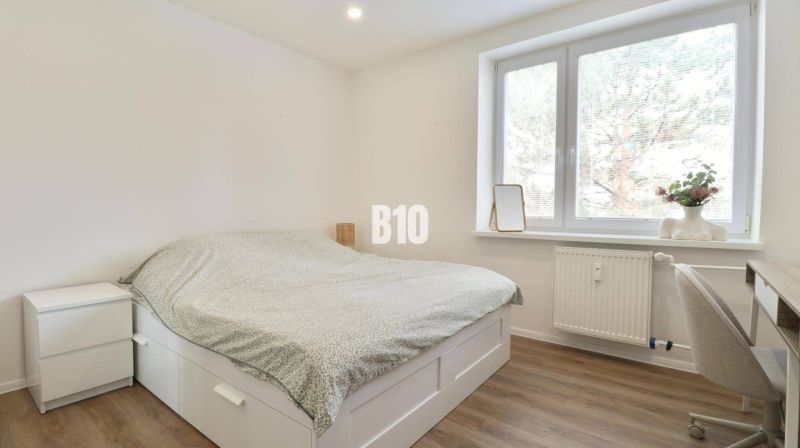 A bedroom in a 3-room apartment with a bed, a desk, and a floor with a wooden decor.