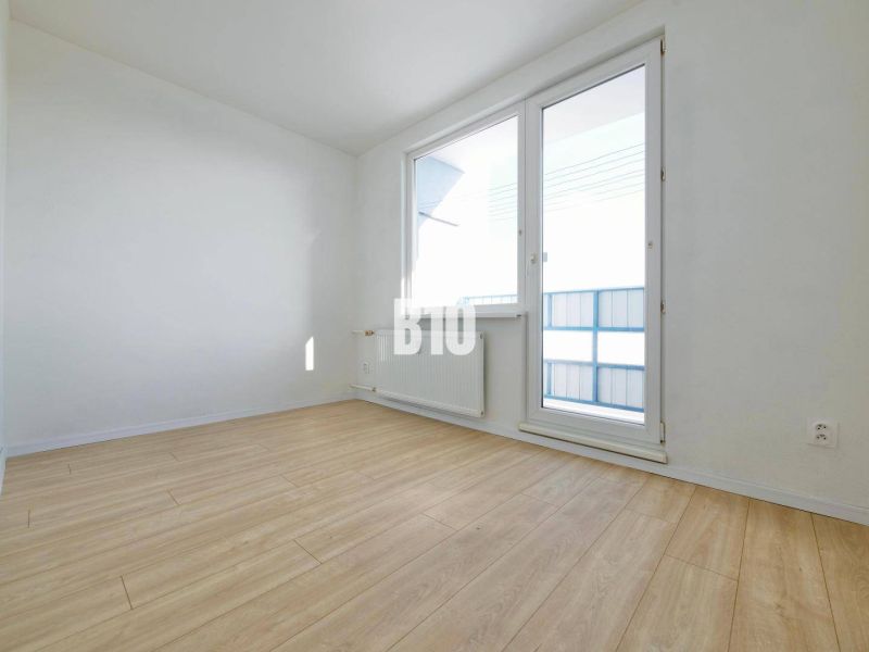 An empty room with a wood-patterned floor, a large window, and white walls.