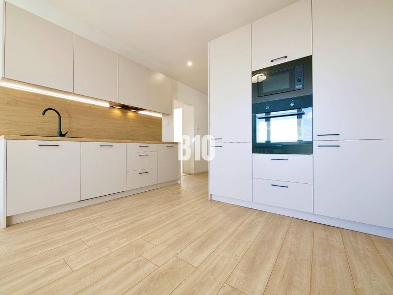 A kitchen in a 3-room apartment with white cabinets and a wood-patterned floor.
