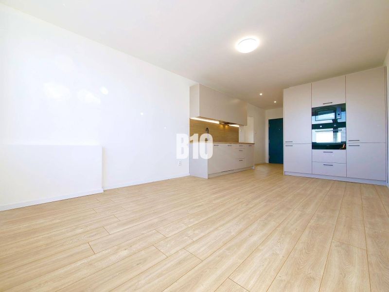 A kitchen in a 3-room apartment with a wood-patterned floor, white furniture, and appliances.