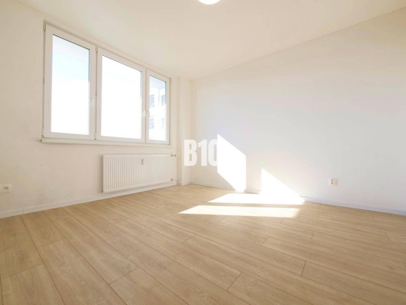 A room in a 3-room apartment with large windows and a floor with a wooden decor.