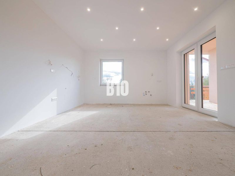 A spacious room with white walls and large windows, awaiting completion in a family house.