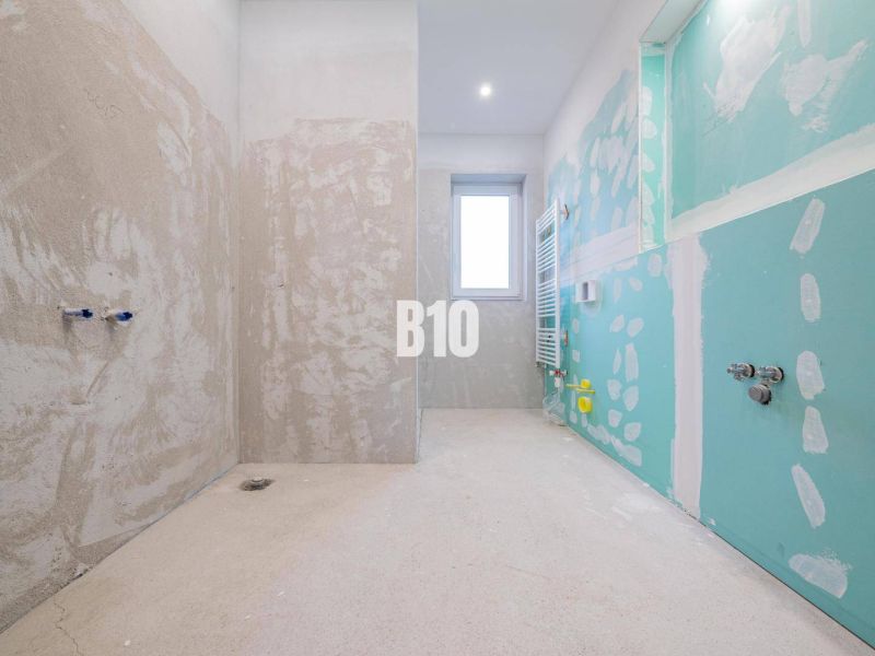 Unfinished bathroom in a family house without tiles, with a window and a radiator.