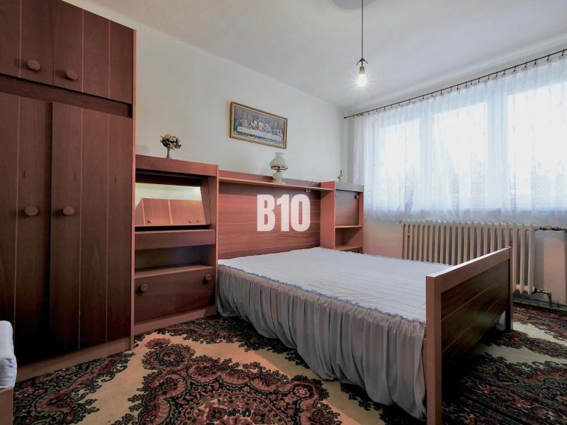 Bedroom in a 3-room apartment with carpet, wooden furniture, and a window with white curtains.
