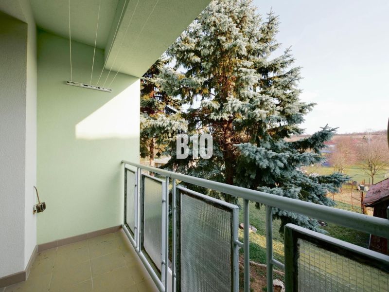 Balcony of a 3-room apartment with a view of greenery and a tree.