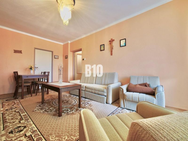 A living room in a three-room apartment with seating and a carpet, furnished in a classic style.
