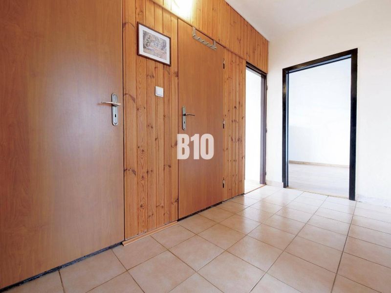 A hallway in a 3-room apartment with tiles, wooden paneling, and entrances to other rooms.