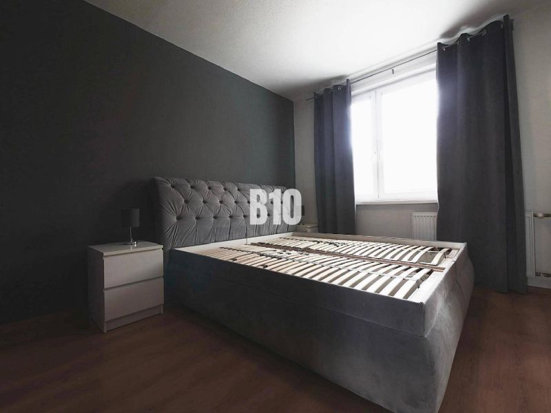 Bedroom with a dark gray bed, nightstand, and wood-patterned flooring in a 3-room apartment.