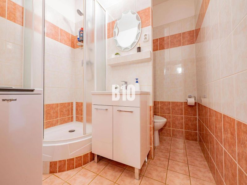 A bathroom in a 2-room apartment with tiles, a shower corner, and a cabinet under the sink.
