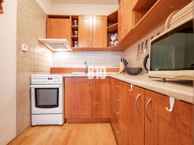 A kitchen in a 2-room apartment with wooden decor flooring and cabinets.