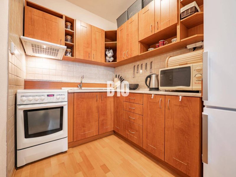 A kitchen with wooden cabinets, white appliances, and a wood-patterned floor in a two-room apartment.