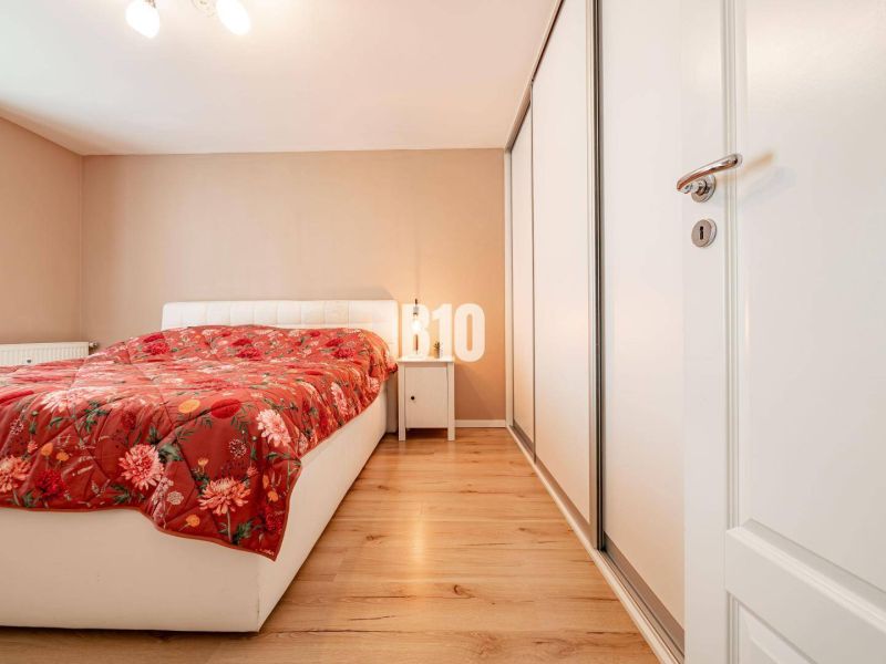 Bedroom in a 3-room apartment with a white bed, floral throw, and wood-patterned flooring.