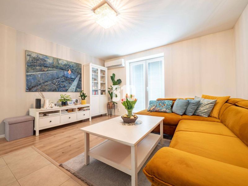 Living room of a three-room apartment with a wooden decor floor and a mustard sofa.