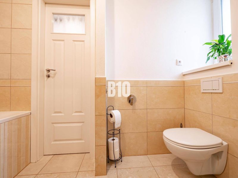 A bathroom with a wall-hung toilet and beige tiles in a 3-room apartment.