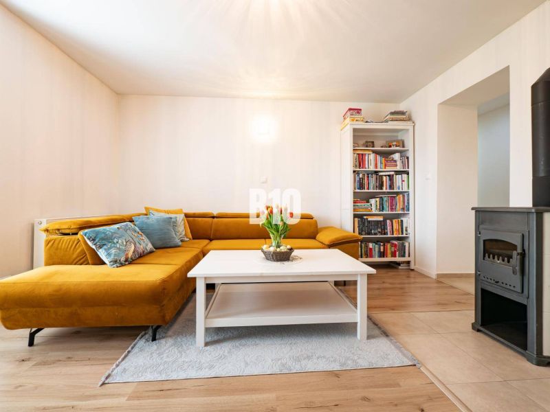 Living room in a 3-room apartment with a mustard sofa, a bookshelf, and a tiled stove.