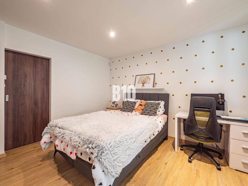 A bedroom in a family house with polka dot wallpaper, a bed, a table, and a wooden decor floor.