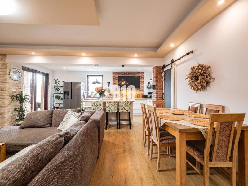 Open space in a family house with a sofa, kitchen, and dining table, wooden decor flooring.