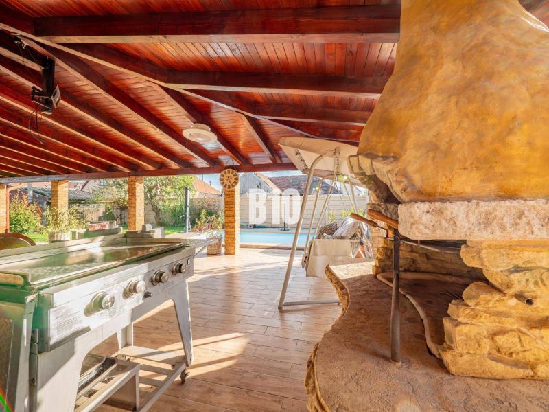 There is a covered terrace with a garden grill and a wooden-patterned floor in the exterior of the family house in Nitra.