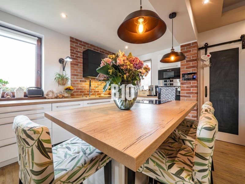 A kitchen in a family house with a dining table, a wooden decor floor, and brick cladding.