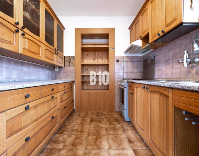 A kitchen in a family house with wooden cabinets and tiled flooring.