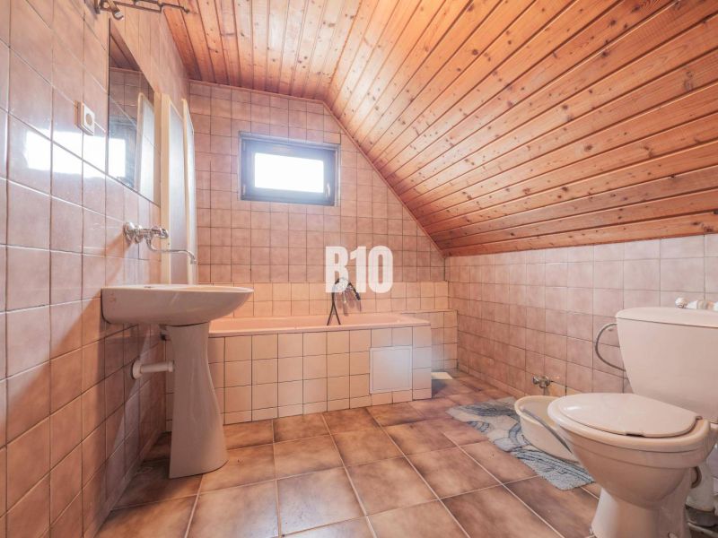 A bathroom in a family house with ceramic tiles and a wooden ceiling.