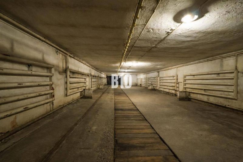 A dark underground space of a production facility with pipes on the walls and lighting.