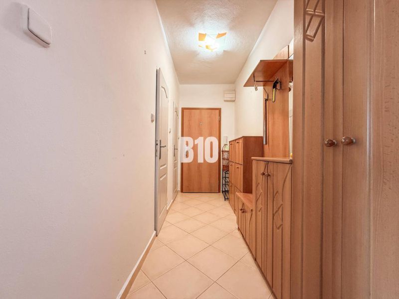 A hallway in a 3-room apartment with wooden storage furniture and tiled flooring.