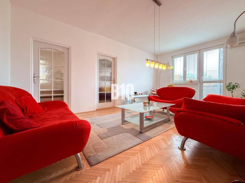 Living room in a 3-room apartment with a red sofa and a floor with a wooden decor.
