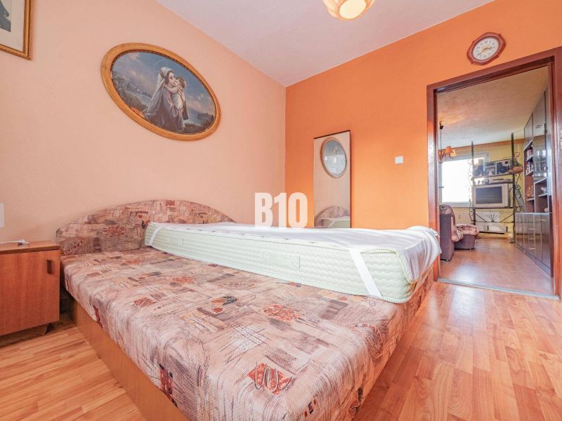 A bedroom with a sofa, a painting, and a wooden decor floor in a 3-room apartment.