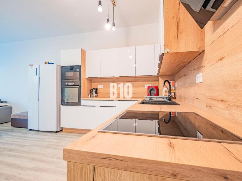 A kitchen in a 3-room apartment with glossy white cabinets and a wood-patterned floor.