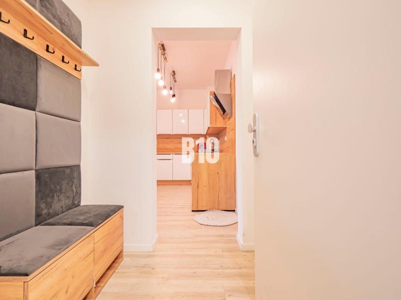 Entrance hallway with seating and view into the kitchen, 3-room apartment with wood-patterned flooring.