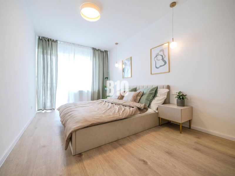 A bright bedroom in a two-room apartment with a wood-patterned floor and minimalist furniture.