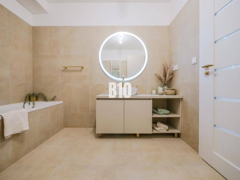 A bathroom with a round mirror and beige tiles in a 2-room apartment.