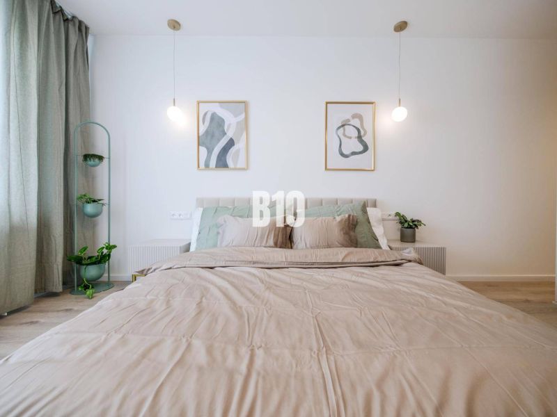 Double bed with green plants and wood-patterned flooring in a two-room apartment.