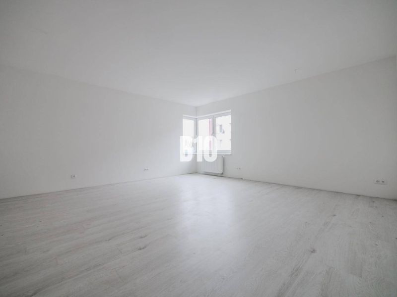 A spacious room with white walls and a large window in a studio apartment.