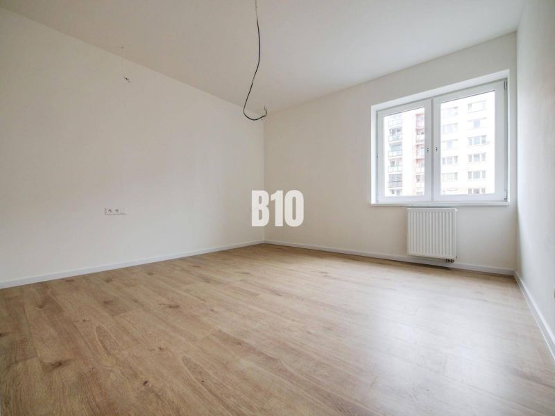 A room in a three-room apartment with a wooden decor floor and a large window.