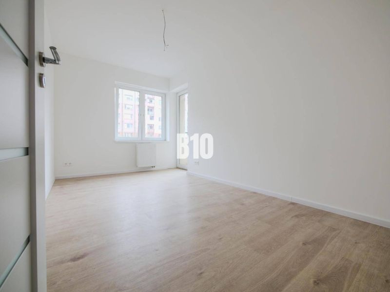 A room with a wooden decor floor in a 3-room apartment and large windows.