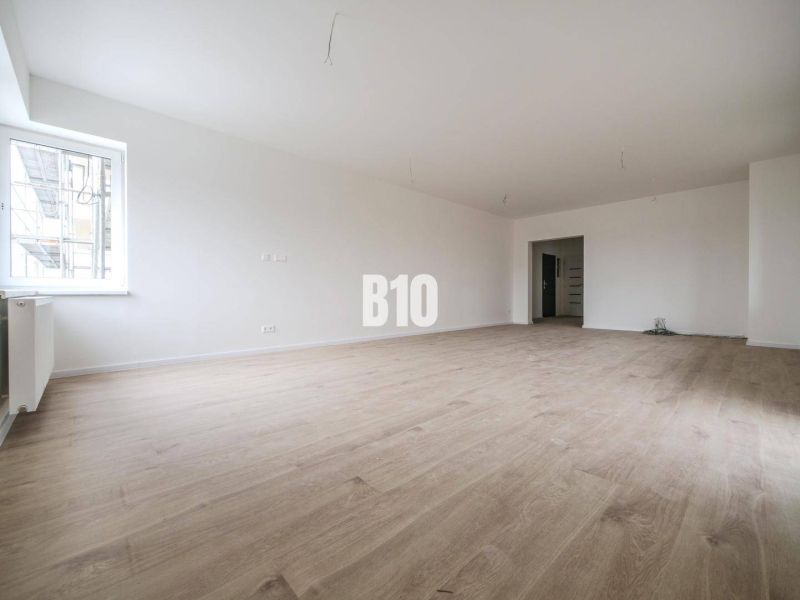 A spacious room in a 3-room apartment with a wooden decor floor and white walls.