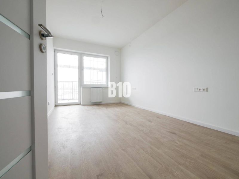 A spacious room with a large window, light flooring, and white walls in a 2-room apartment.
