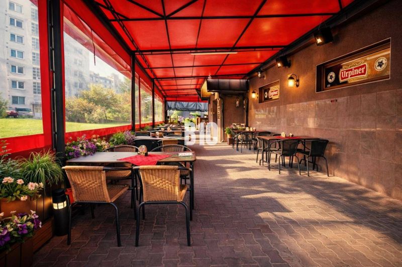 An outdoor terrace of a building in Čadca with tables, a red roof, and greenery.