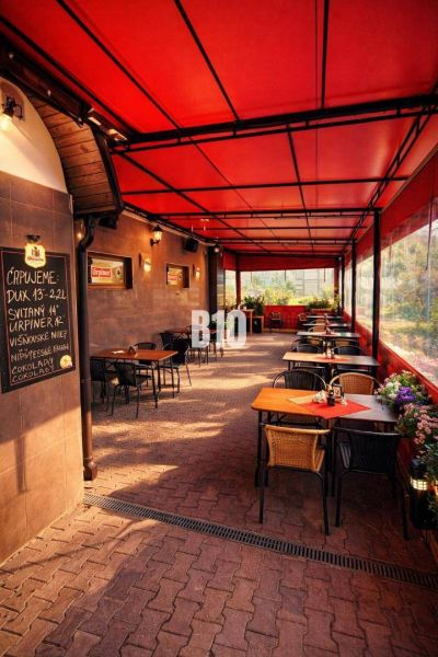 Covered terrace of a restaurant in the building of the town Čadca with brick paving, flowers, and tables.
