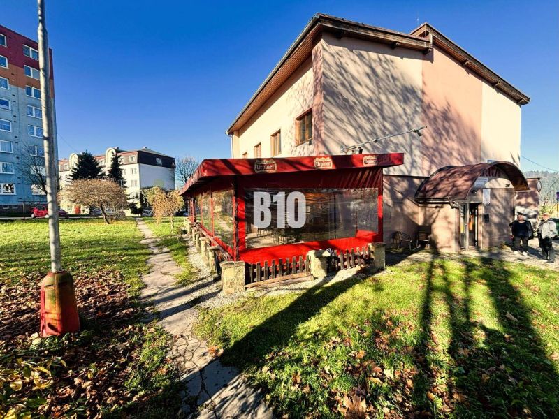 A building in Čadca with a garden, terrace, and red awning in sunny weather.