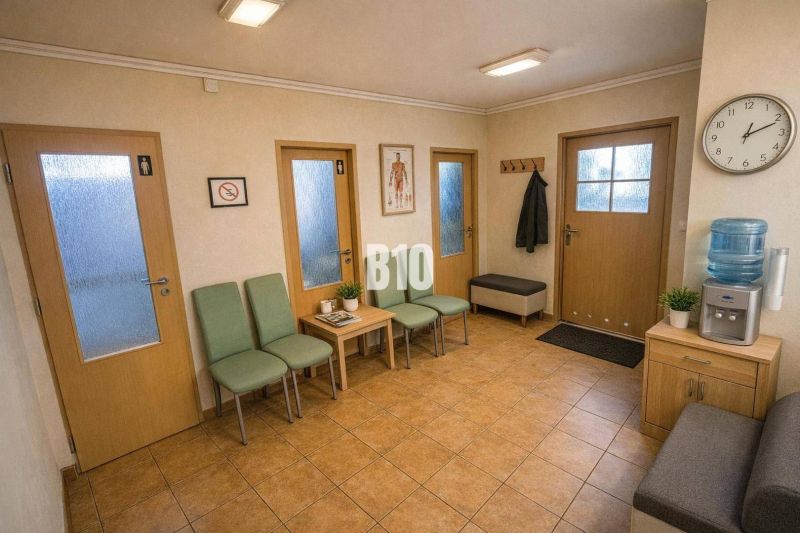 A waiting room with green chairs, magazines, and a clock. A floor with ceramic tiles.