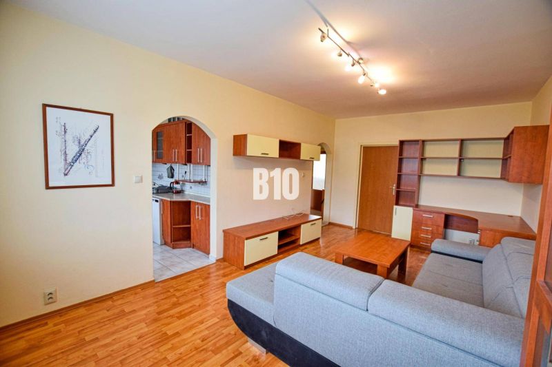 Living room with wood-patterned flooring in a 3-room apartment, connected to the kitchen.