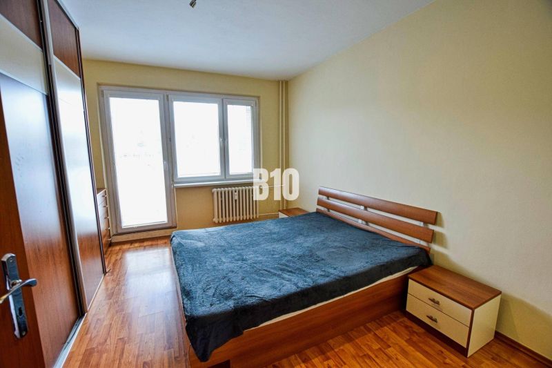 A bedroom in a 3-room apartment with a bed, wood-patterned flooring, and a built-in wardrobe.