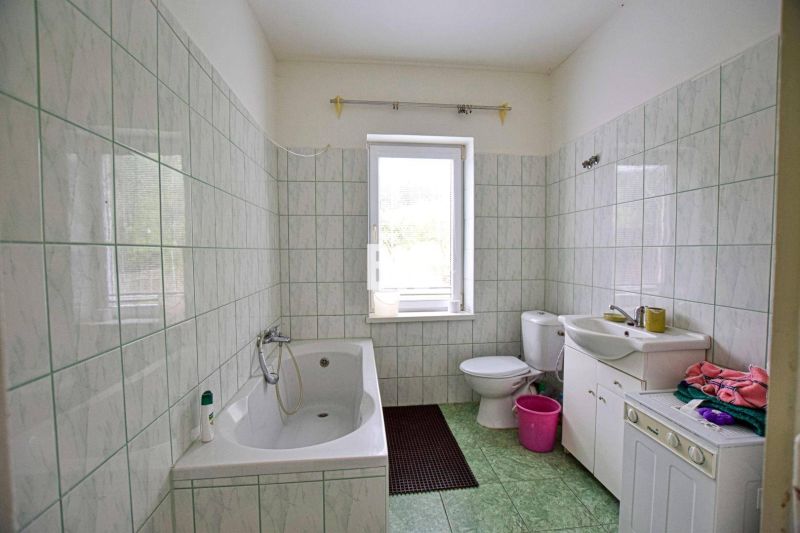 A bathroom in a family house with a bathtub, sink, and washing machine, tiled with light tiles.