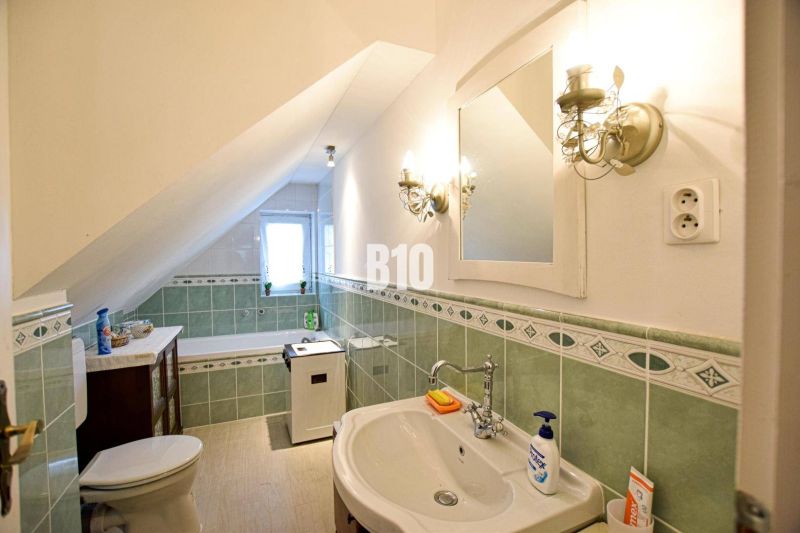 A bathroom in a family house with green tiles and an attic ceiling.