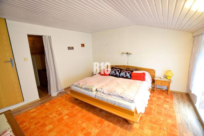 A bedroom in a cottage with a bed, curtains, and an orange carpet.