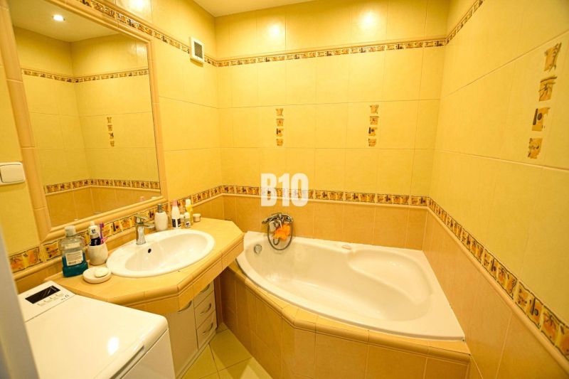 Bathroom with yellow tiles, a bathtub, a sink, and a mirror in a 3-room apartment.