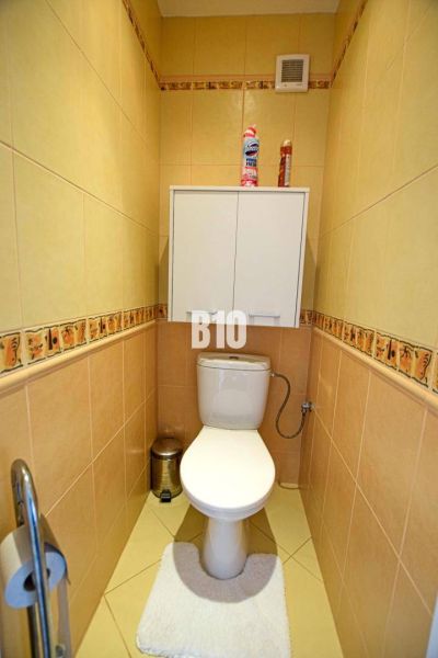 A toilet with beige tiles and a wall cabinet in a 3-room apartment.